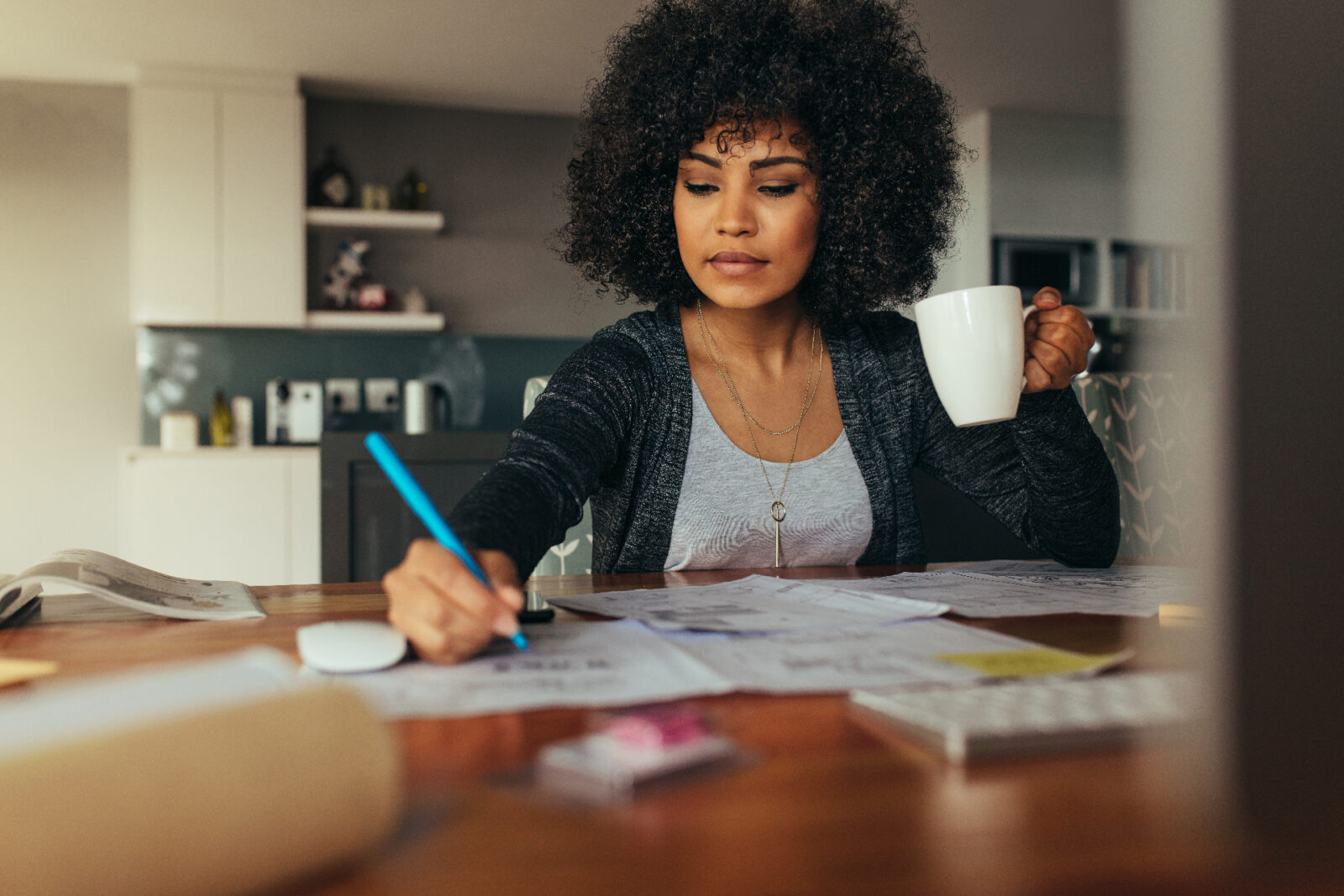 Female working from home at table writing with coffee in hand