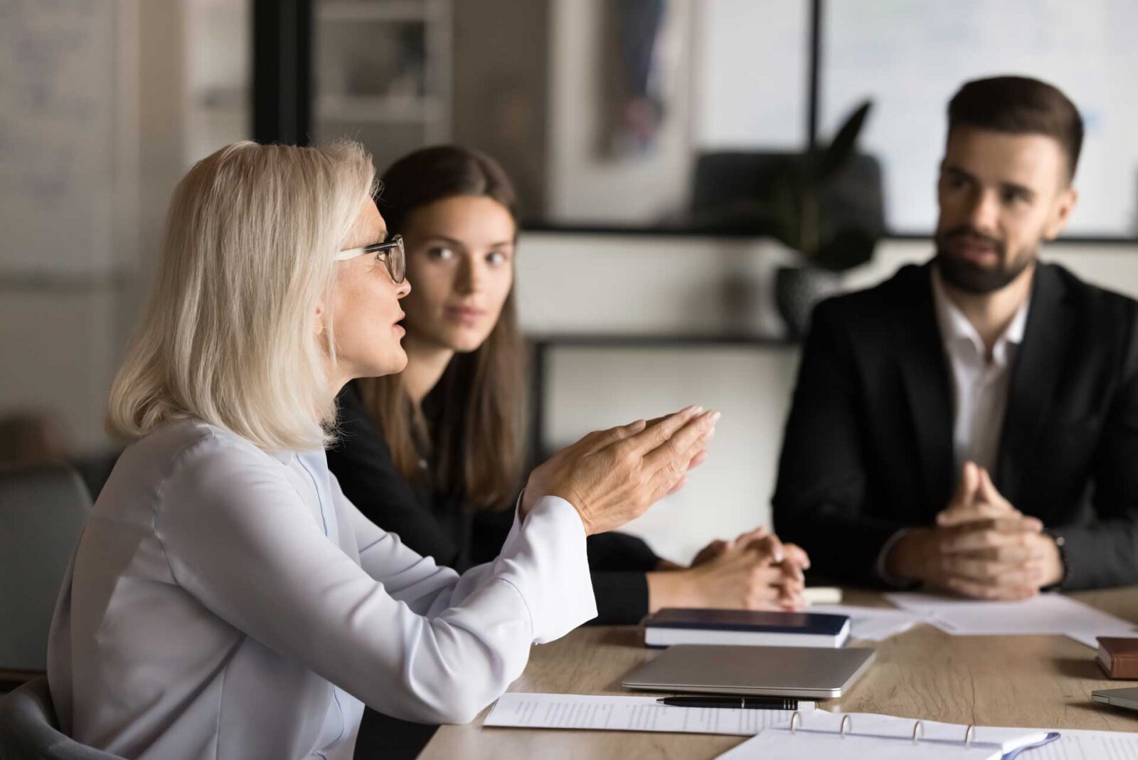 Blonde senior business professional woman talking to younger colleagues on brainstorming meeting