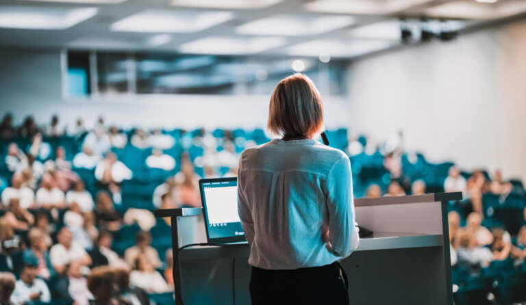 Behind stage view of female speaker giving a talk at corporate business conference