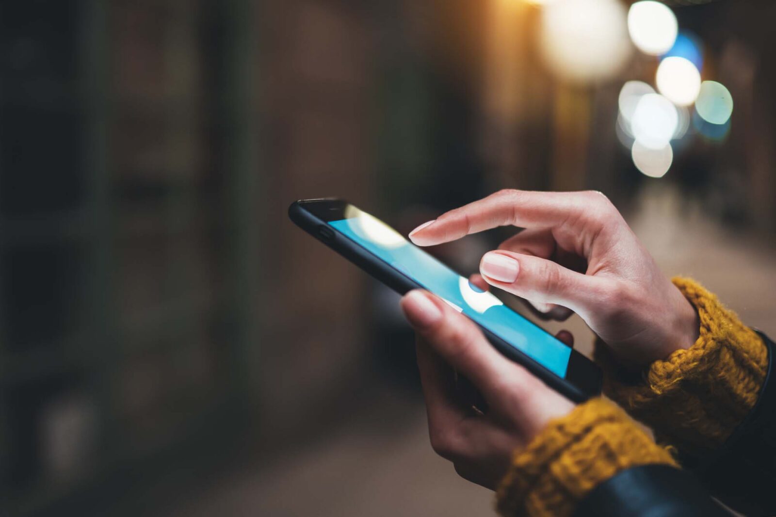 Close up of finger pointing at smart phone screen with city lights in background