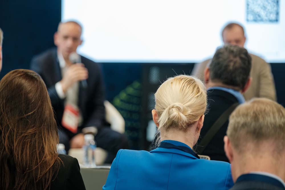 Audience seated at a business panel event, looking towards speakers presenting on stage